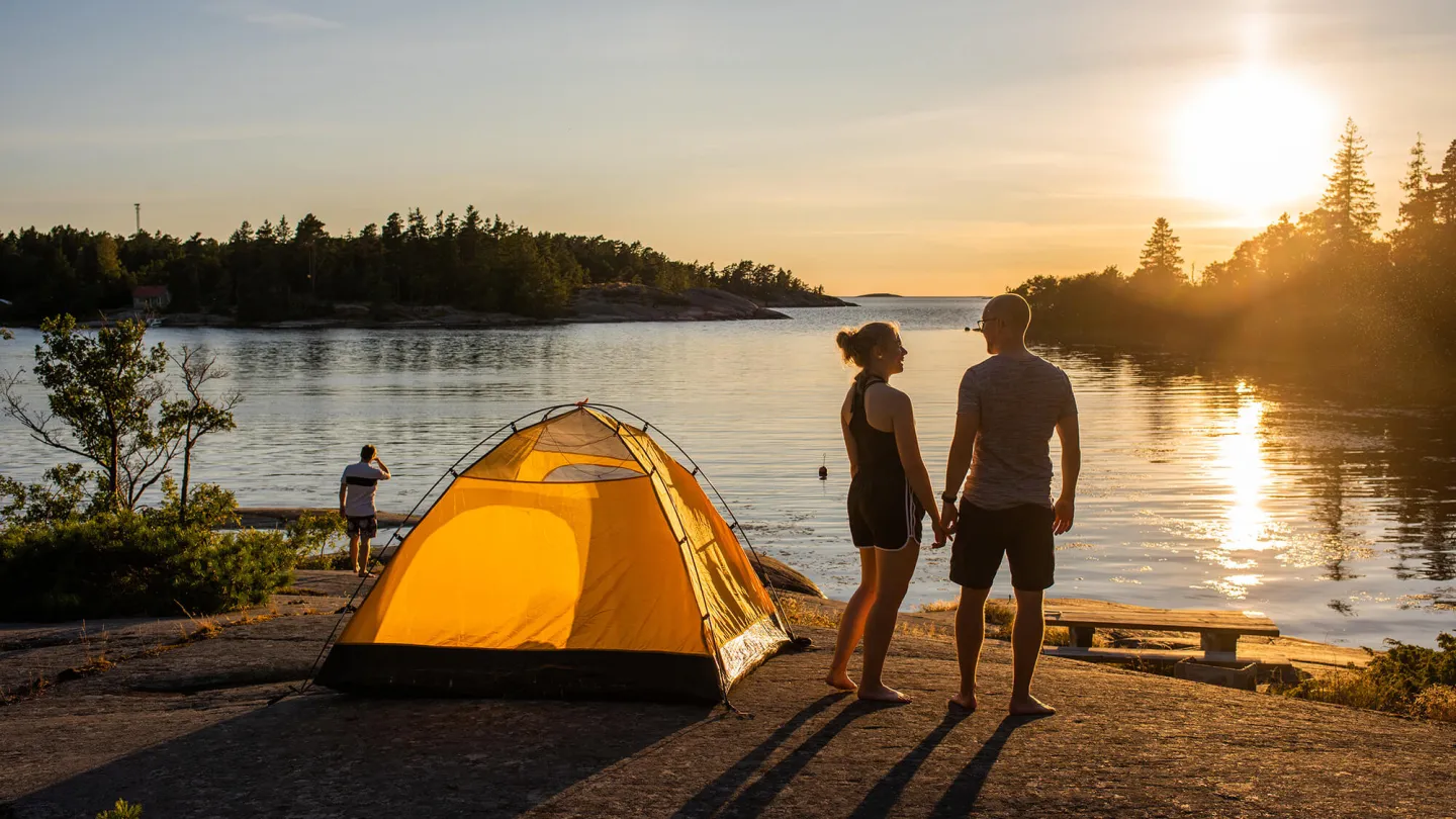 Två personer som står vid sitt tält och kollar på solnedgången